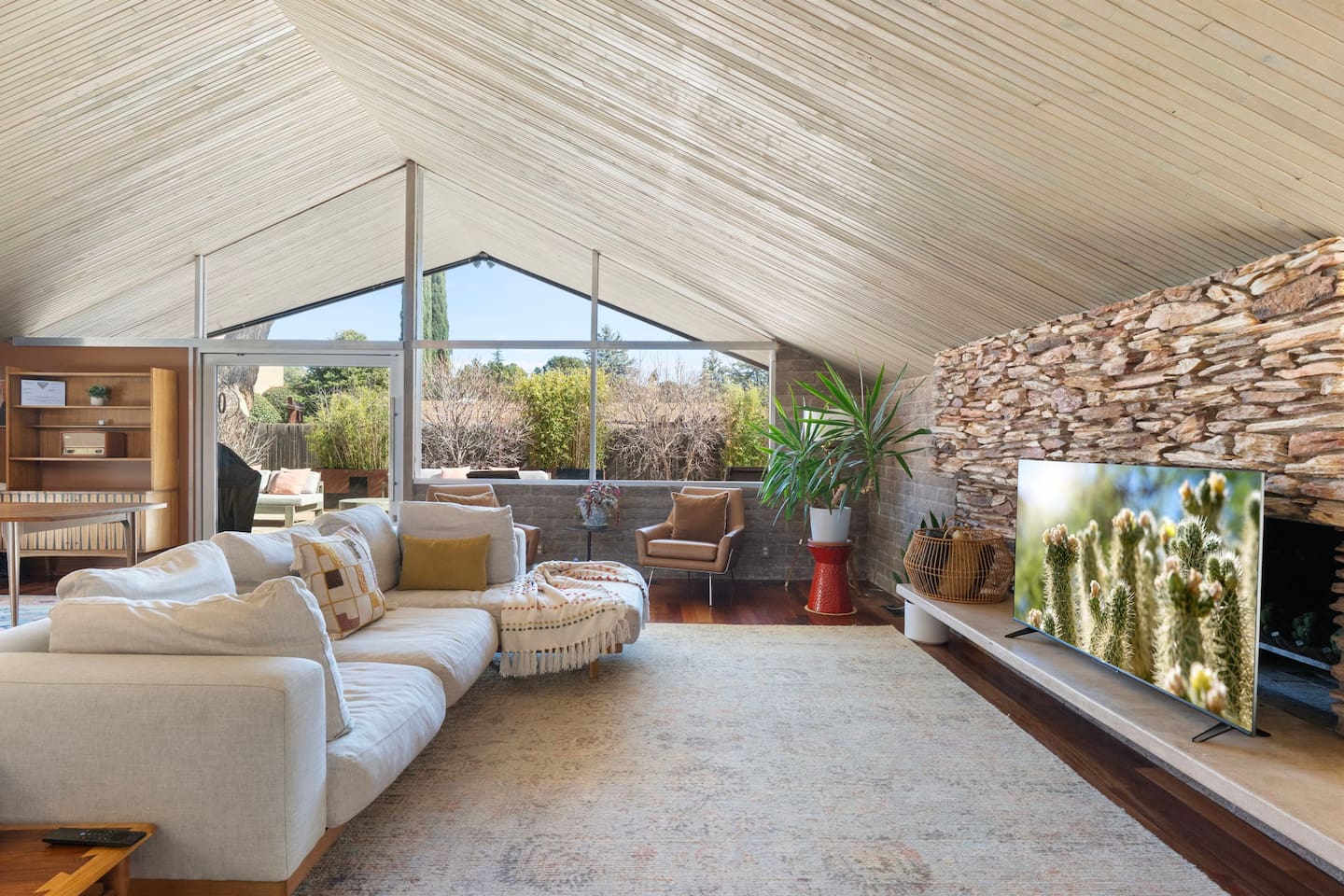 Bright, open living room with vaulted wood ceilings, floor-to-ceiling windows, and a cozy oversized sectional—perfect for relaxing after a day of exploring.