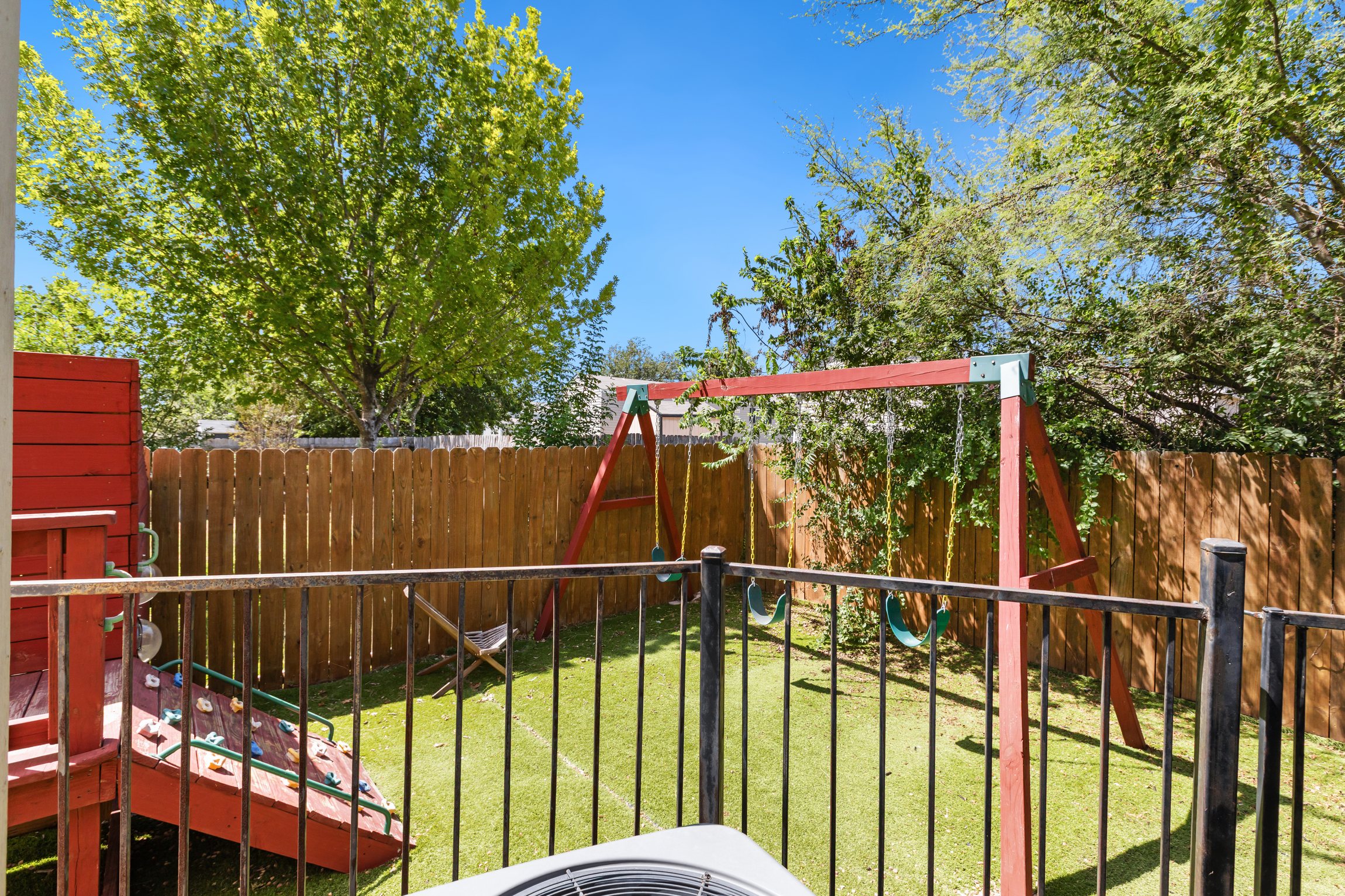 Private backyard playground and swing set on green grass, viewed from the pool deck. Fully fenced yard keeps kids safe. A family-friendly outdoor setup that makes this San Antonio rental perfect for trips with young kids.