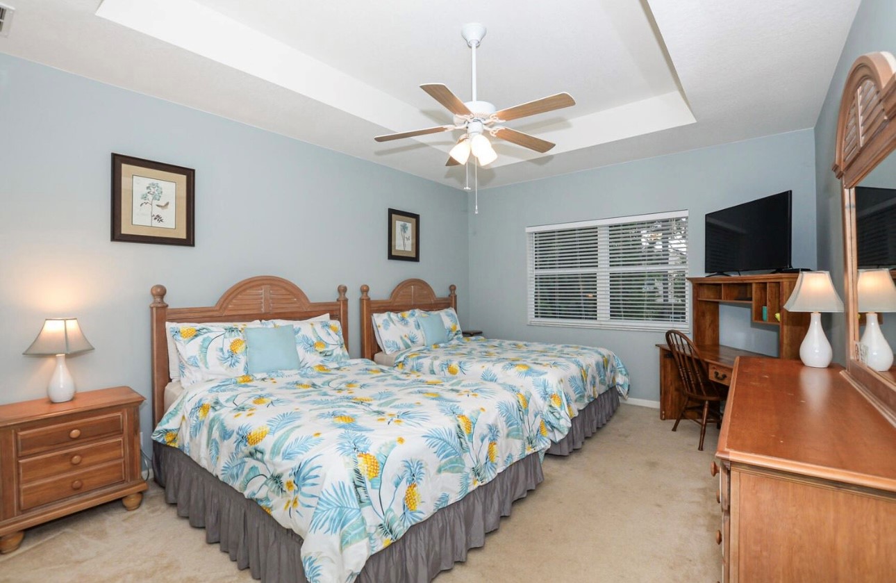 Comfortable bedroom featuring a large bed, ceiling fan, dresser storage, TV, and natural light.