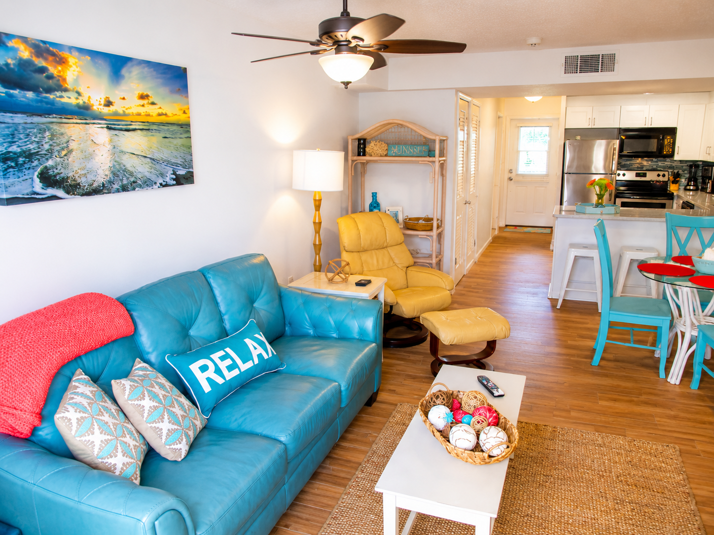 Coastal living room with turquoise sofa, vibrant accents, and modern kitchen for a relaxing stay.