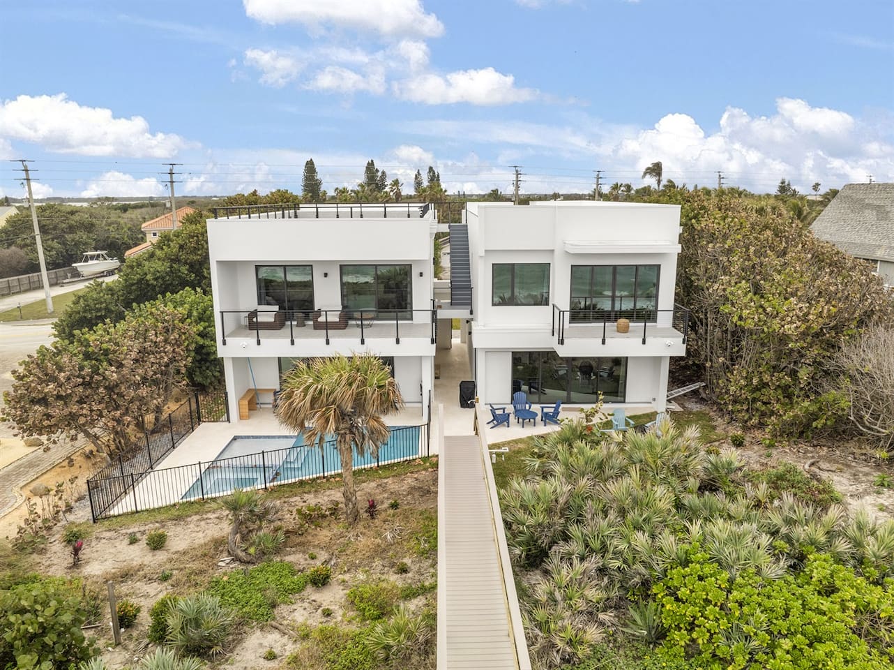 Captured by drone, this outdoor space features a beautifully designed swimming pool, surrounded by lush trees and greenery, with a charming bridge leading to the sea, creating a serene and inviting ambiance for relaxation.