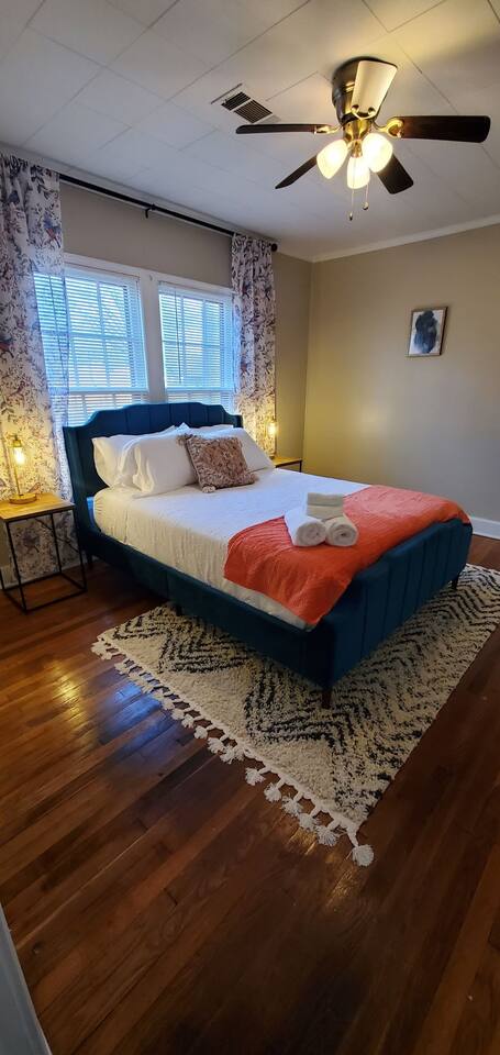 Bright and cozy bedroom featuring a stylish upholstered bed, vibrant decor, fresh towels, and natural light—ideal for relaxing and unwinding.