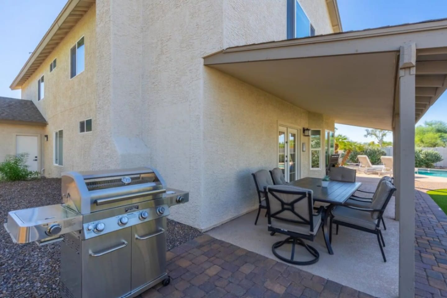 Outdoor kitchen and dining area with gas grill, covered patio, and pool views—ideal for entertaining.
