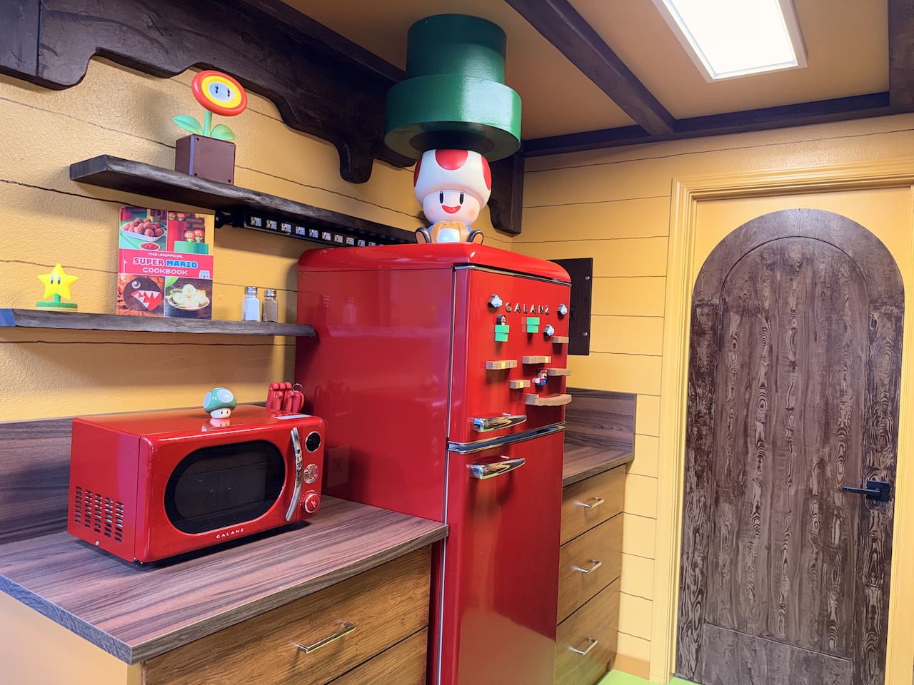Full Mario kitchen corner featuring the bright red retro fridge and microwave at Mario's Mini Mansion, Clermont, FL. Toad figurine on top and fun shelves complete this vibrant, family-friendly cooking space. Wooden door leads to a Yoshi's Fort room!