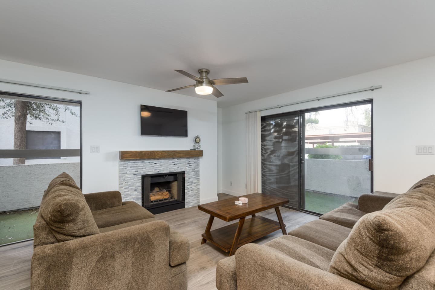 Living room with soft seating, a fireplace, wall-mounted TV, and patio doors on both sides.
