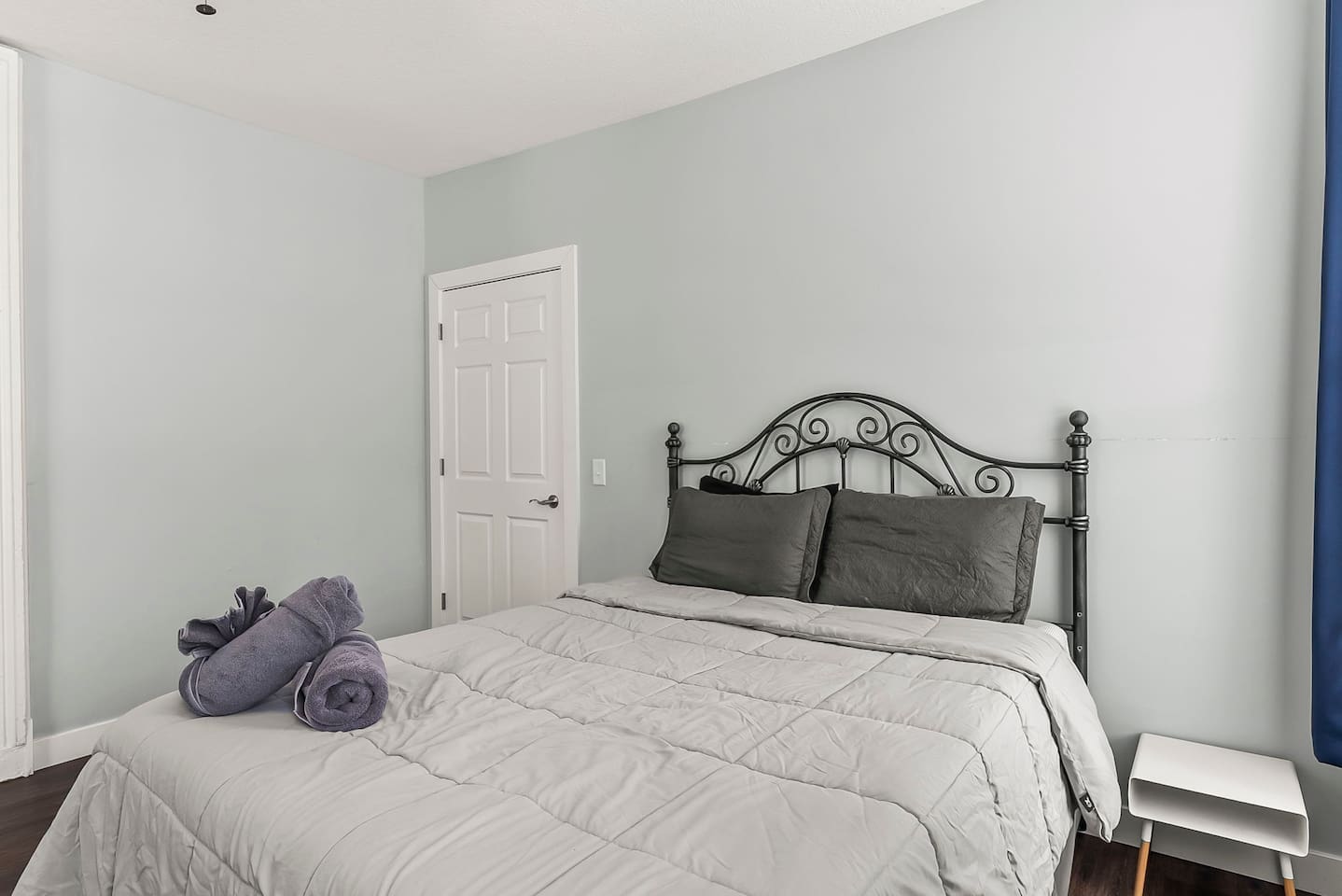 Cozy sleeping space with queen-size bed, side table, and tall windows that fill the room with daylight.