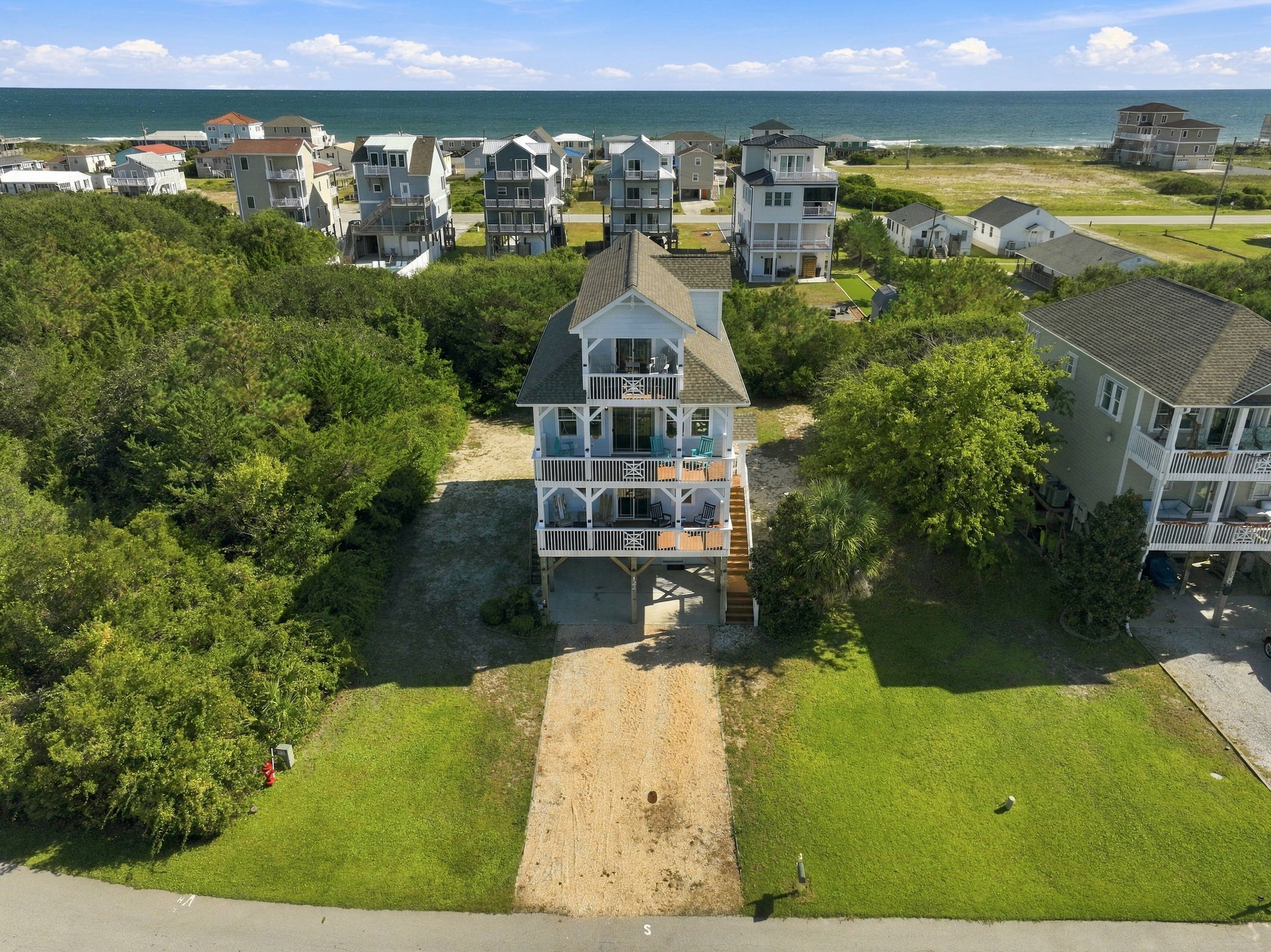 Aerial view of the home surrounded by lush coastal greenery, featuring a spacious driveway and multiple outdoor decks