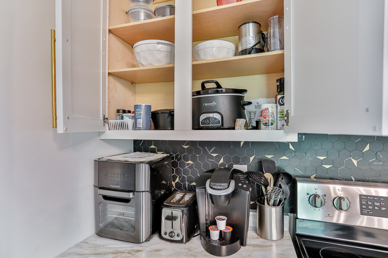 A modern kitchen equipped with high-end appliances and ample lighting. It has a coffee maker, oven, stove top, utensils, and all it takes to fix a delicious meal.
