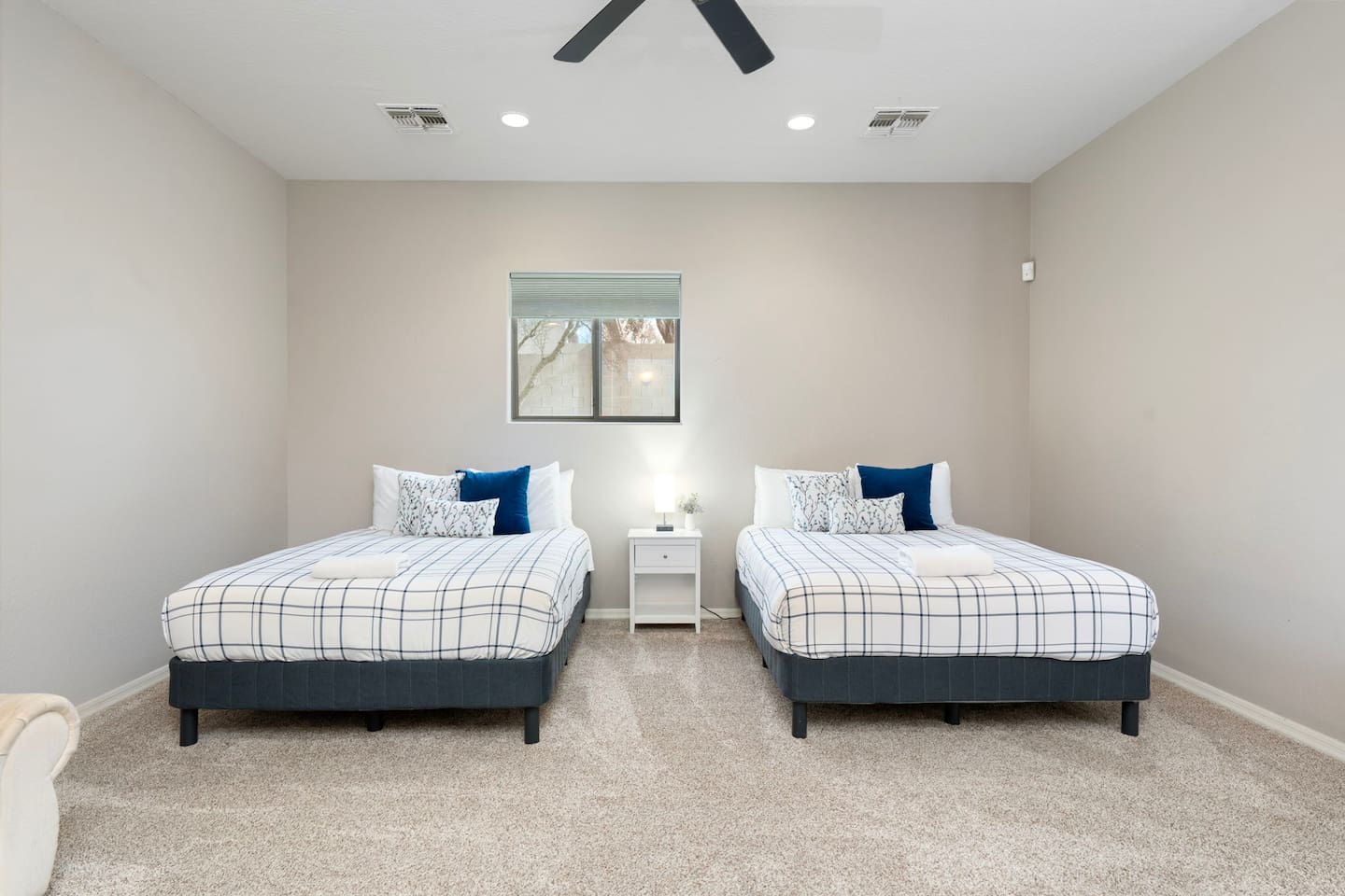 Spacious casita bedroom with two queen beds, ceiling fan, and soft neutral tones—perfect for families or groups needing extra sleeping space.
