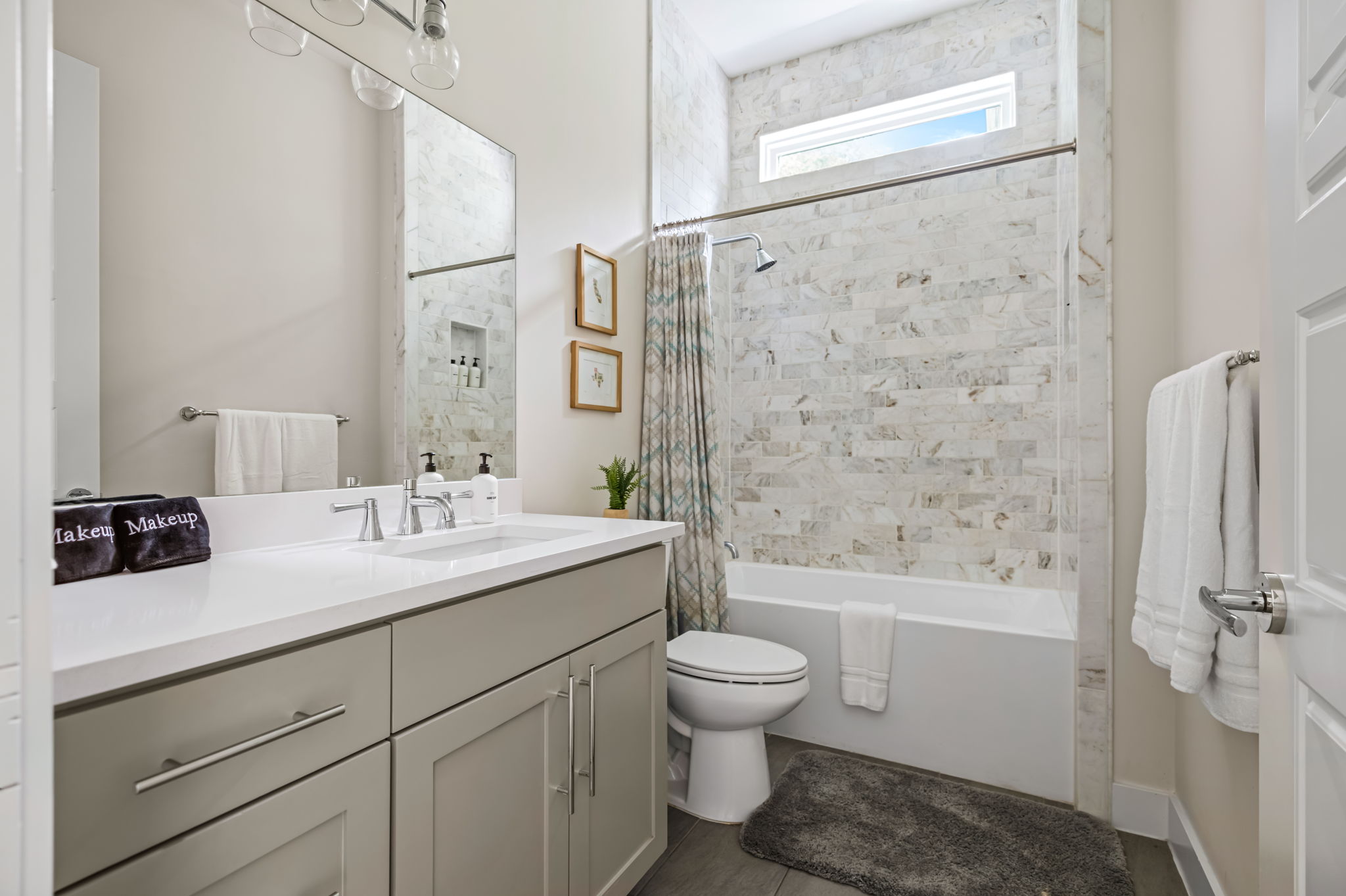 Elegant full bathroom with marble accent wall, soaking tub with shower, and stylish vanity — a spa-like retreat for guests.