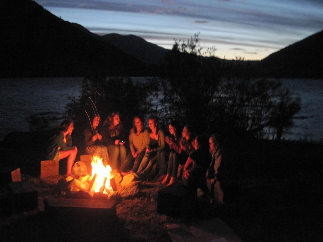 Family sitting around the firepit beside the lake at dusk