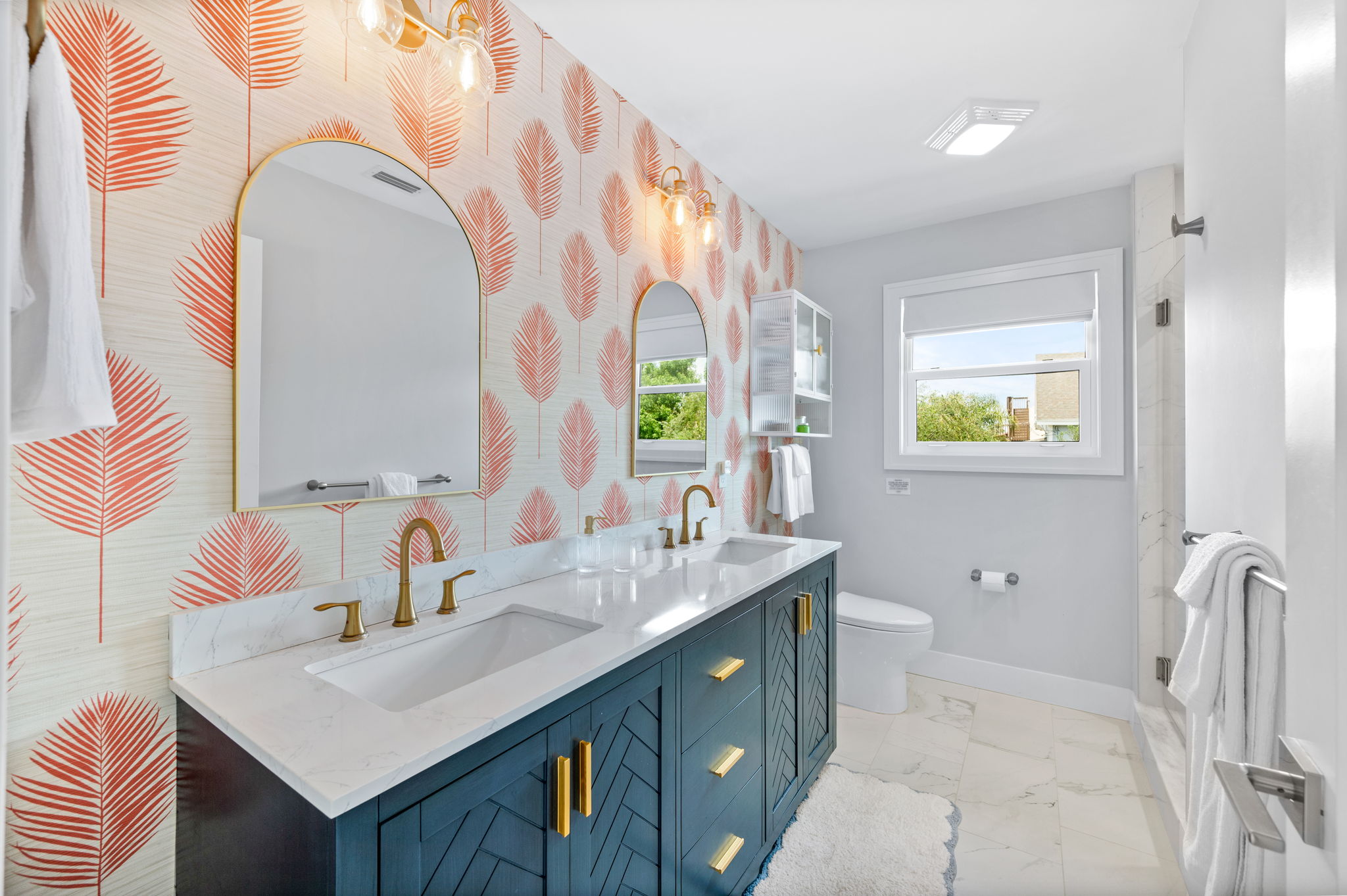 A touch of tropical elegance! The master bathroom features a double vanity and charming coral palm wallpaper, adding a pop of color to the sleek white marble and creating a relaxing, stylish retreat.