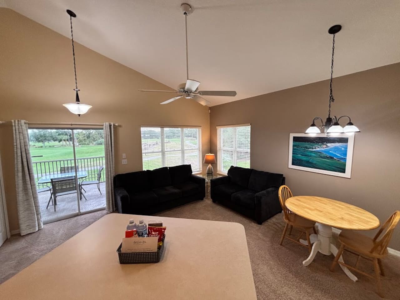 Bright living and dining space with cozy seating, vaulted ceilings, and peaceful views from the balcony doors.