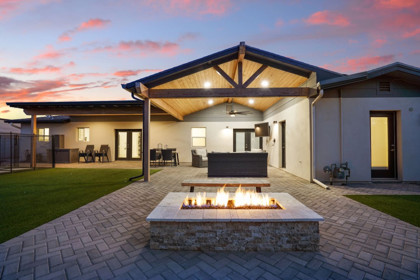Backyard fire pit area with covered lounge seating, warm patio lighting, and sunset views.