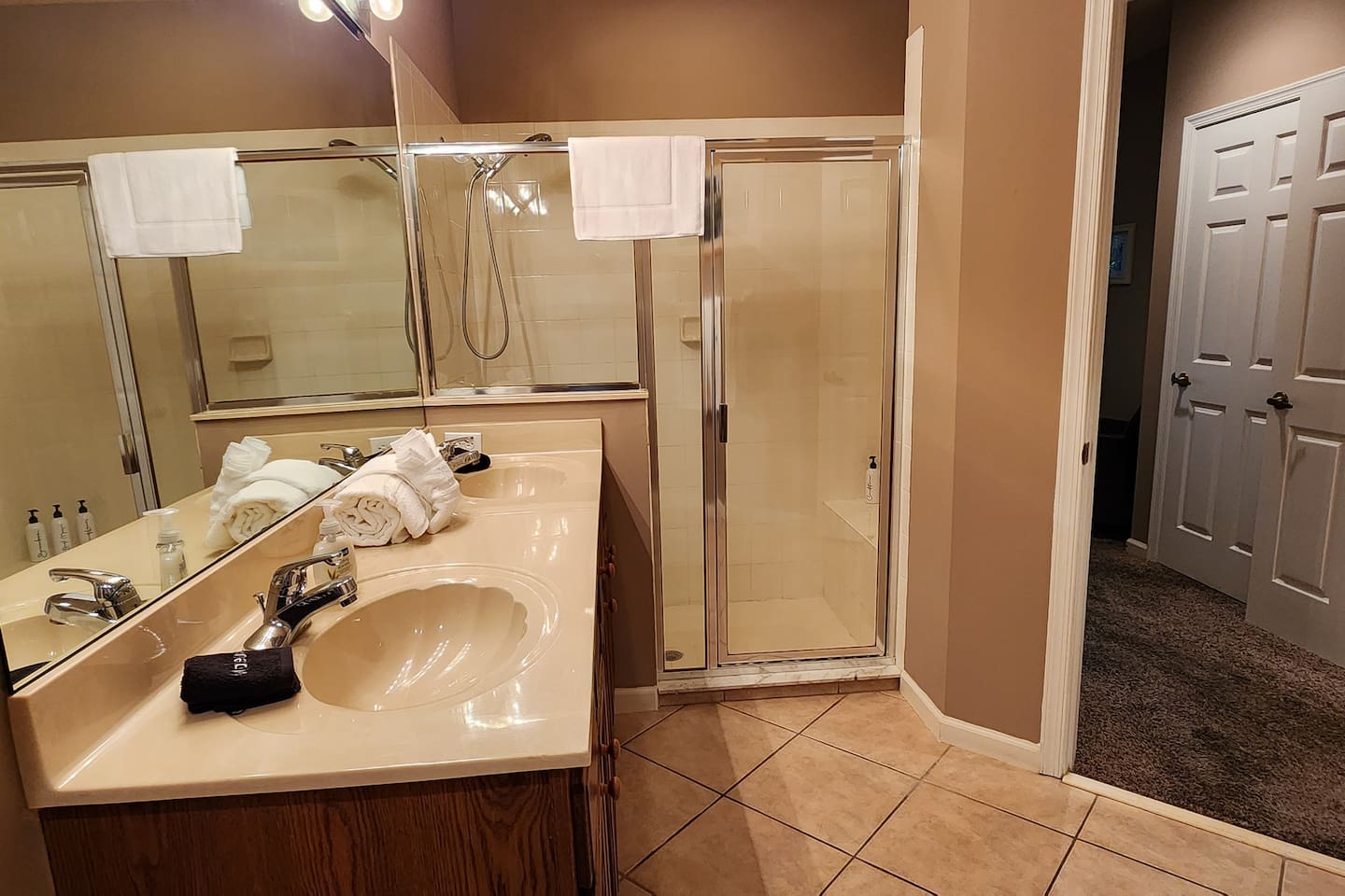 Bright bathroom with a large vanity, walk-in shower with glass doors, and tile flooring.