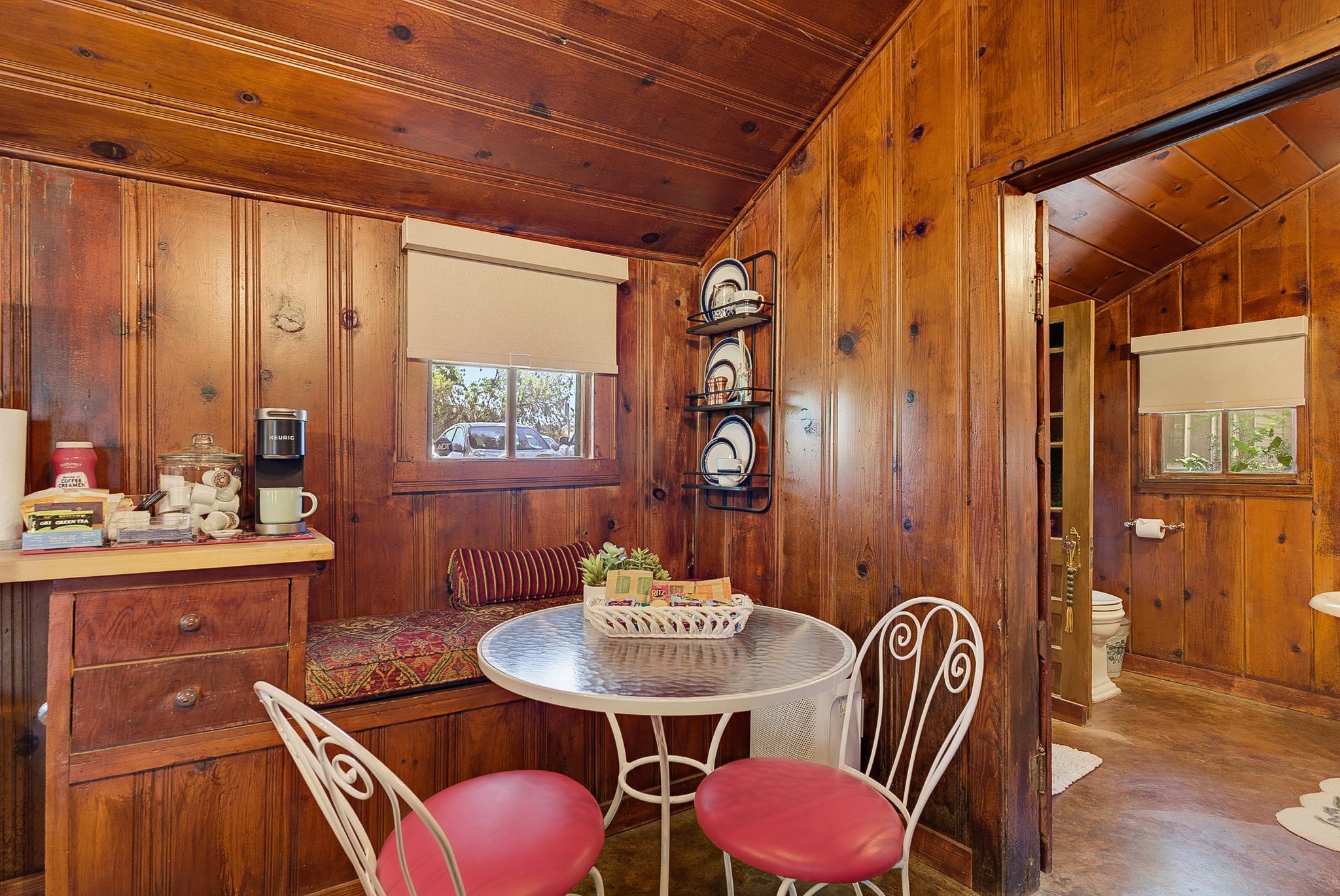 Papaw's Cabin breakfast nook with Keurig coffee station, cushioned bench seating, and knotty pine walls. Charming 1930s log cabin rental in Waco, Texas.