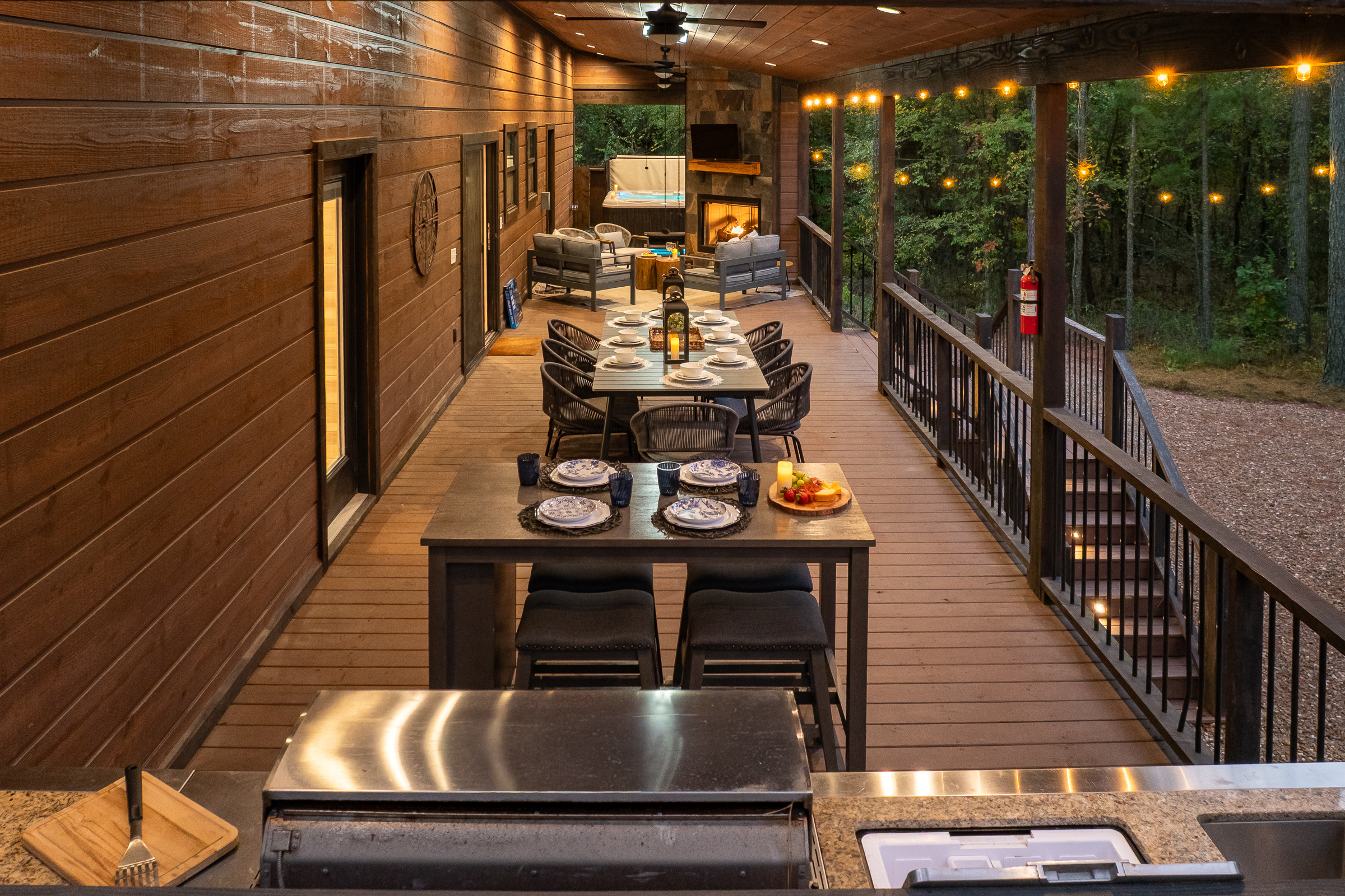 Dusk settles over the glowing wraparound porch, where string lights, cozy seating, and forest views set the tone for unforgettable evenings.