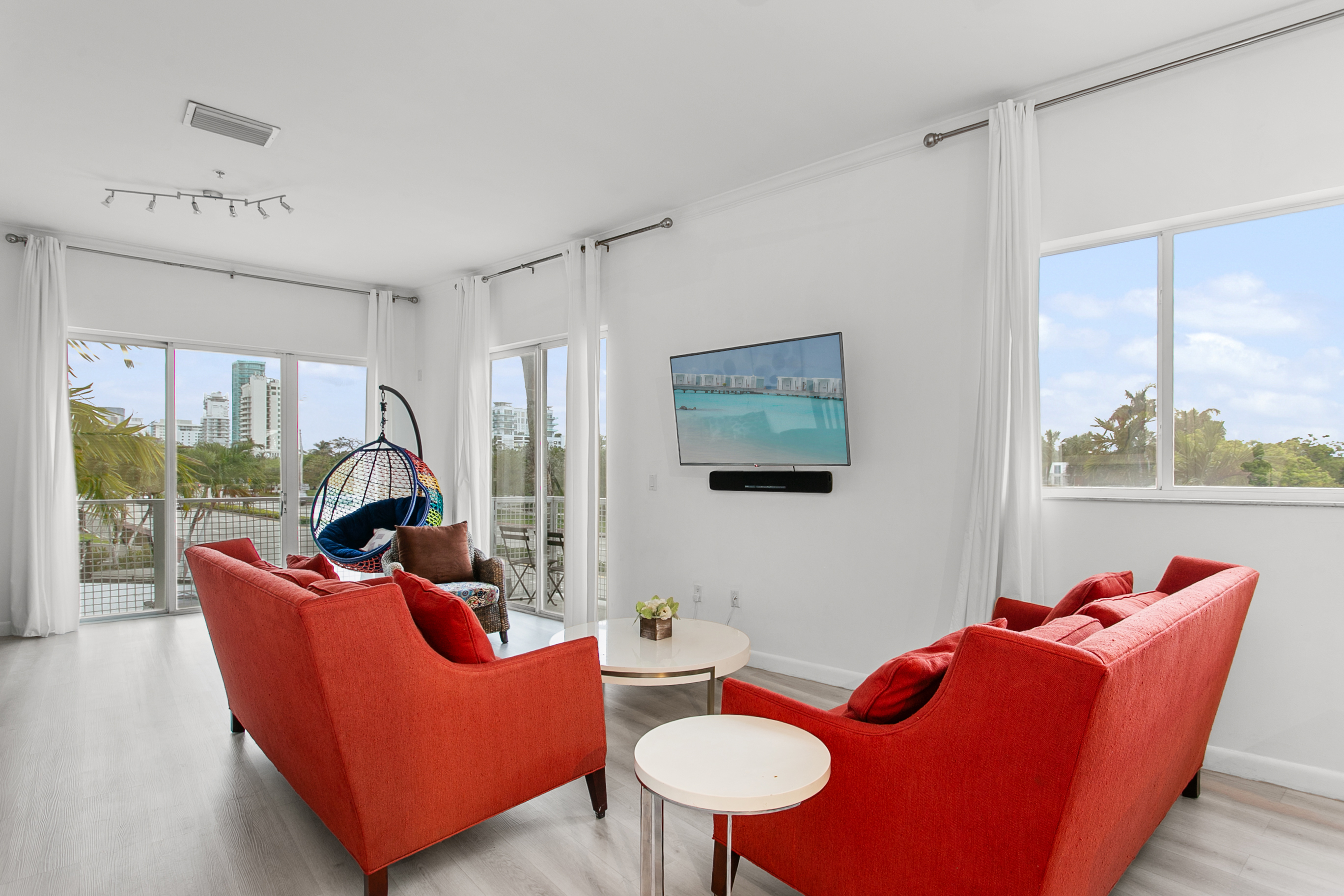Huge sunny corner living room with two sofas, a daybed, and a swing chair. Private balcony with city and waterway views.