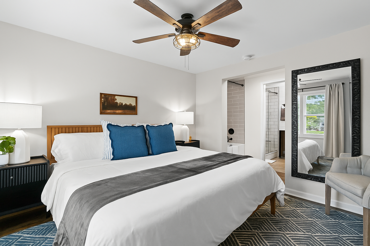 Elegant king bedroom with full-length mirror, ceiling fan, and cozy touches for a restful night’s sleep.