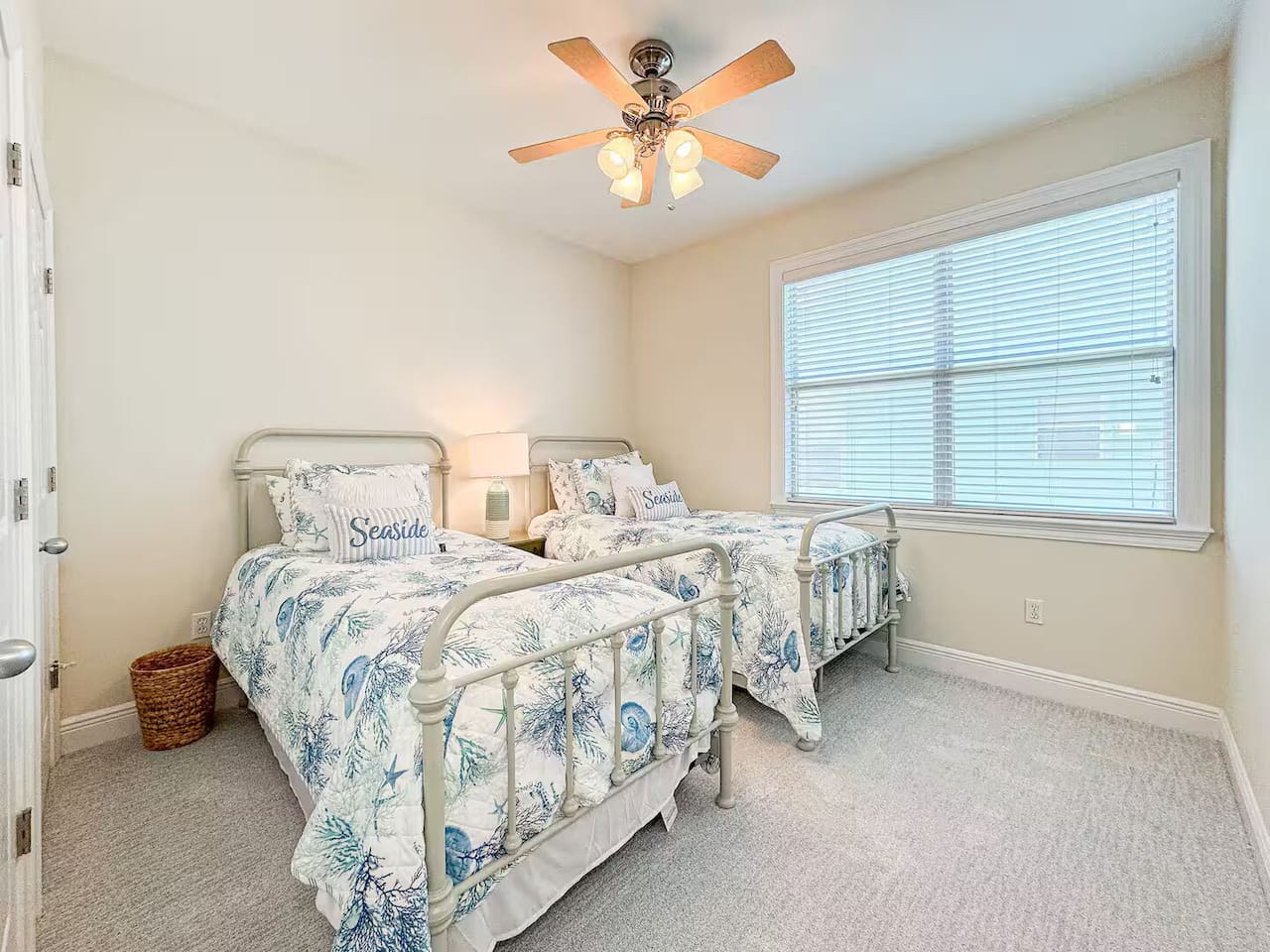 Bright guest bedroom with two twin beds, coastal-themed linens, and plenty of natural light. Includes a ceiling fan and cozy setup—perfect for kids or friends.