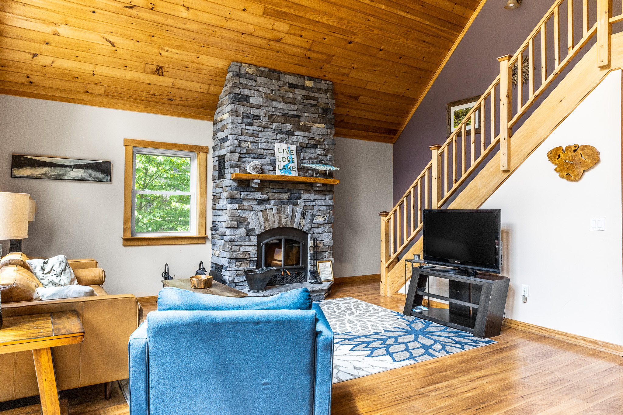 Living room with floor to ceiling stone fireplace (wood not provided). Comfortable leather couch, Roku TV, fast Starlink WIFI, huge windows overlooking the lake.