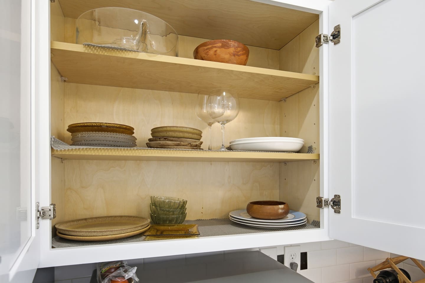 Stocked kitchen cabinets with dishes, plates, bowls, and wine glasses ready for guest use.