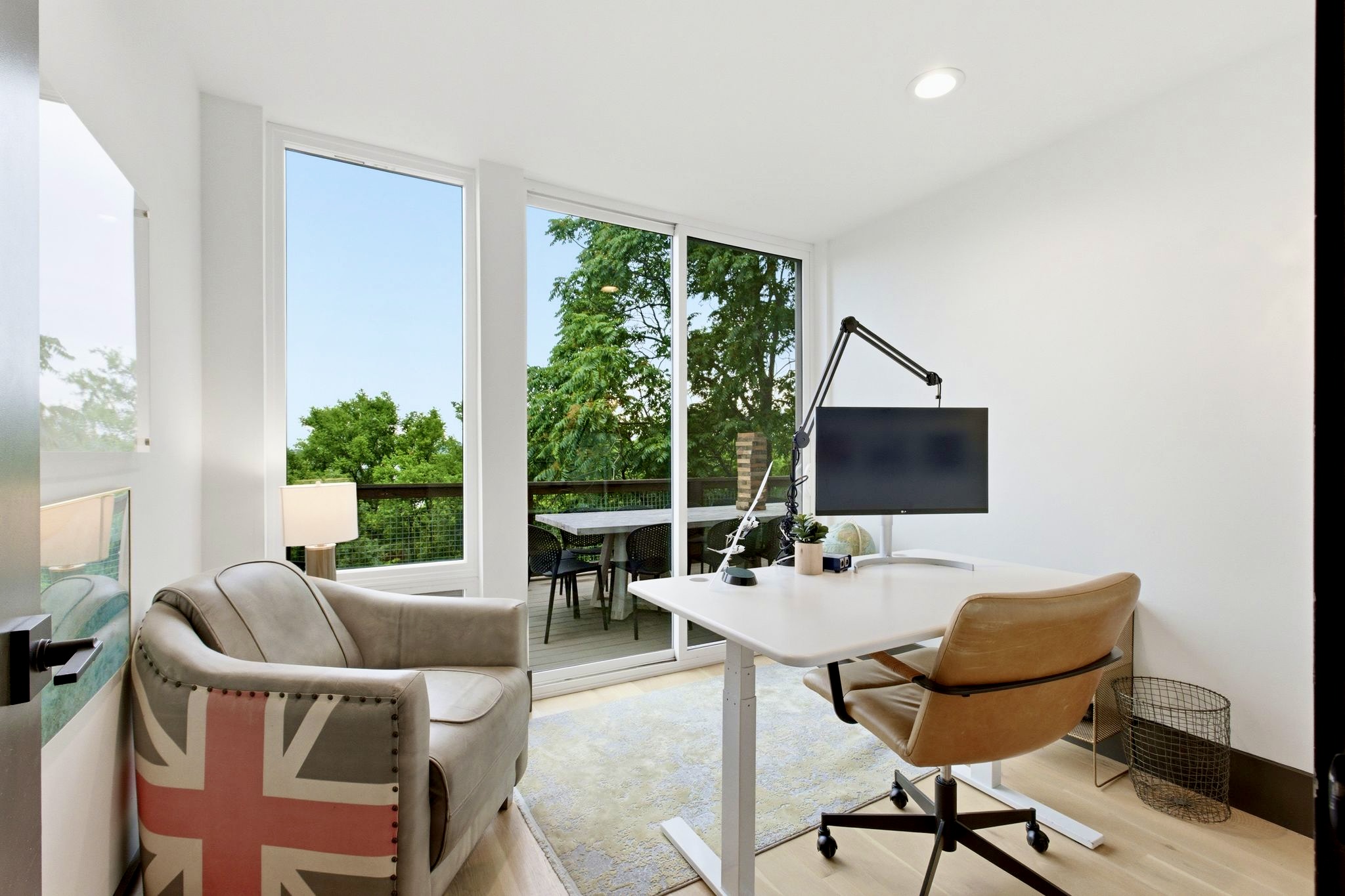 Minimalist home office w/ a wood desk, Eames-style chair & leafy garden views to spark focus.
