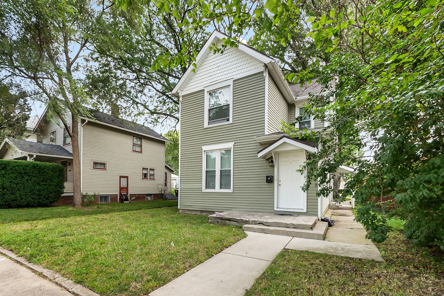 A classic two-story home tucked beneath mature trees on a quiet, tree-lined street.