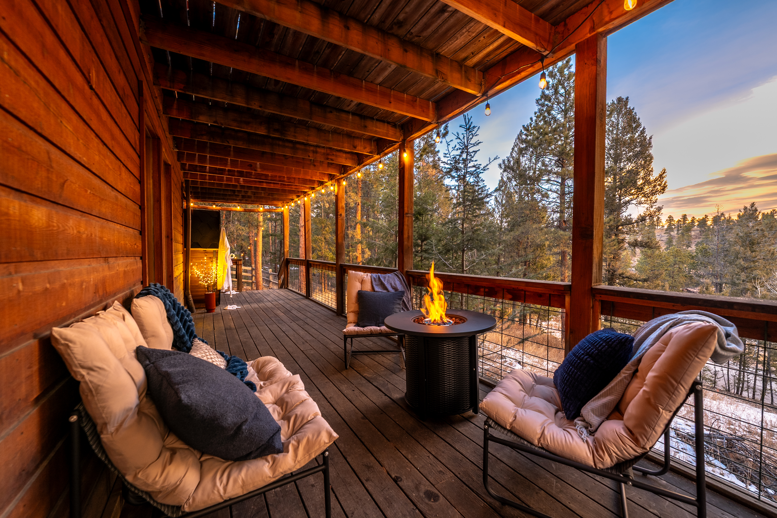 🌅🔥 Golden-hour deck vibes—string lights ✨, cushy lounge chairs, and a glowing fire table with sweeping pine views 🌲 Perfect for sunset sips and cozy nights outside 🥂