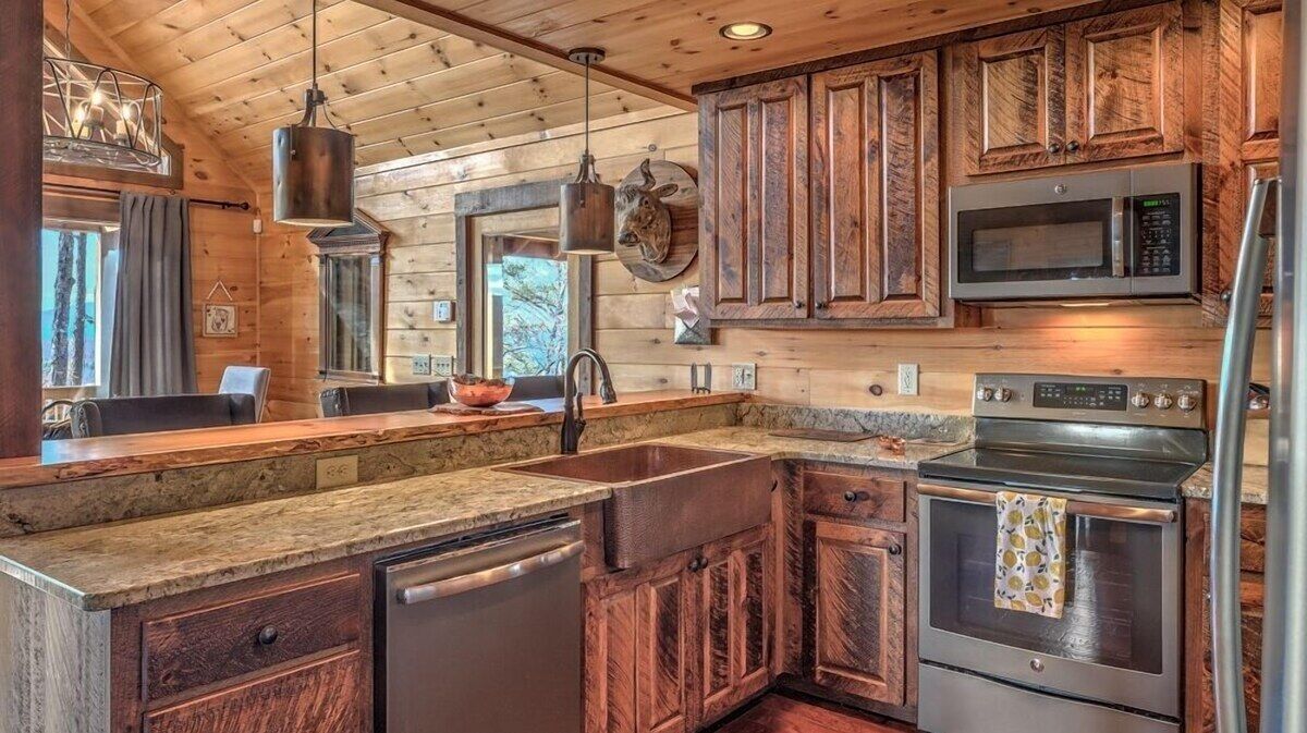 Fully equipped mountain kitchen with rustic wood cabinetry, stainless appliances, farmhouse sink and stone countertops - ready for family meals and group gatherings.