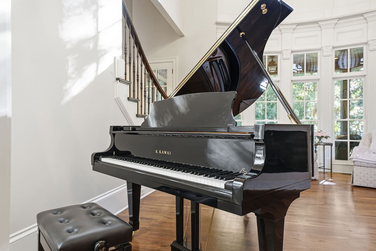 Beautiful entry sitting room with a grand piano, warm fireplace, tall windows, and two comfortable chairs. A bright, serene spot to unwind or enjoy quiet moments.