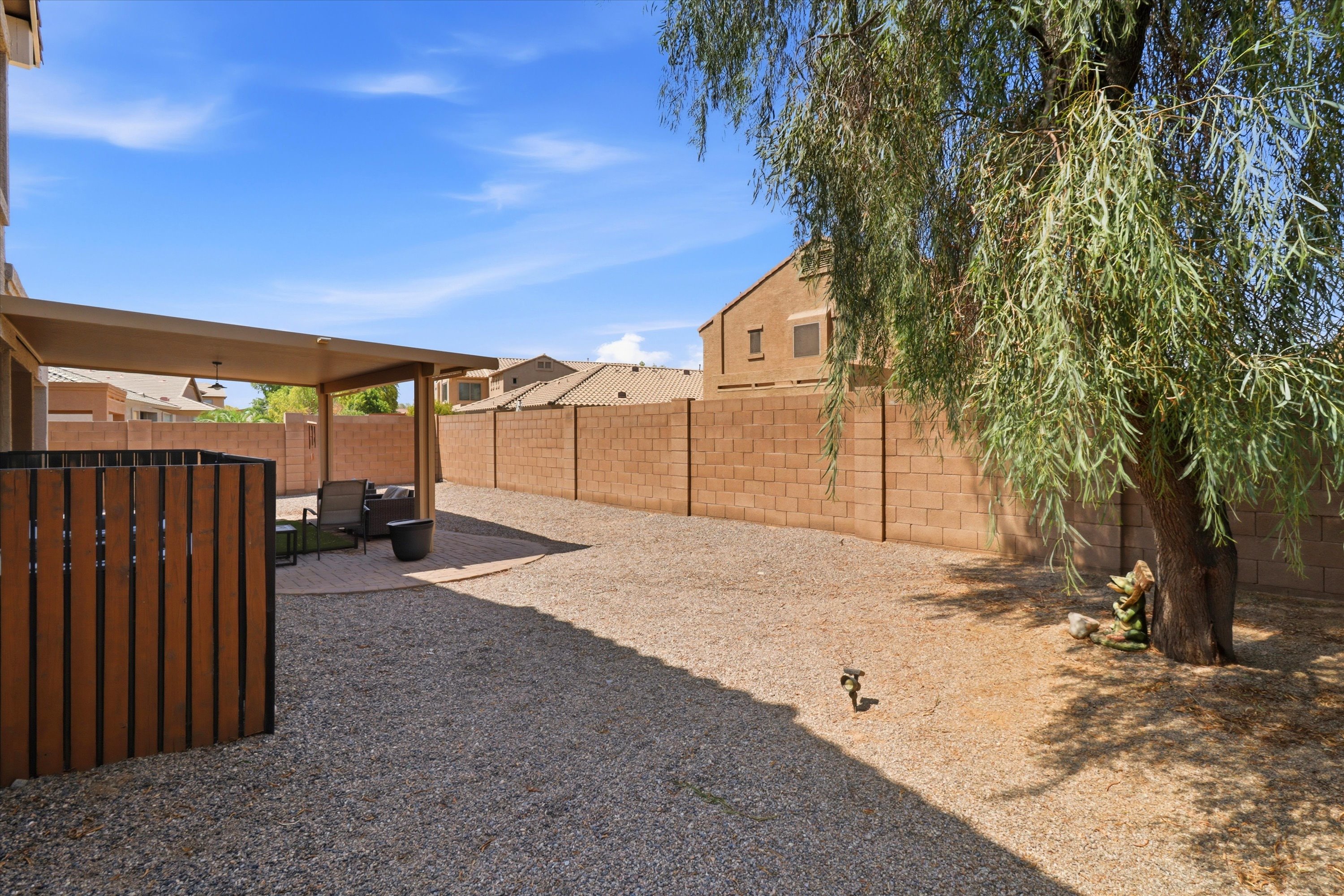 Backyard with a wide gravel yard, shade tree, and covered patio seating nearby.
