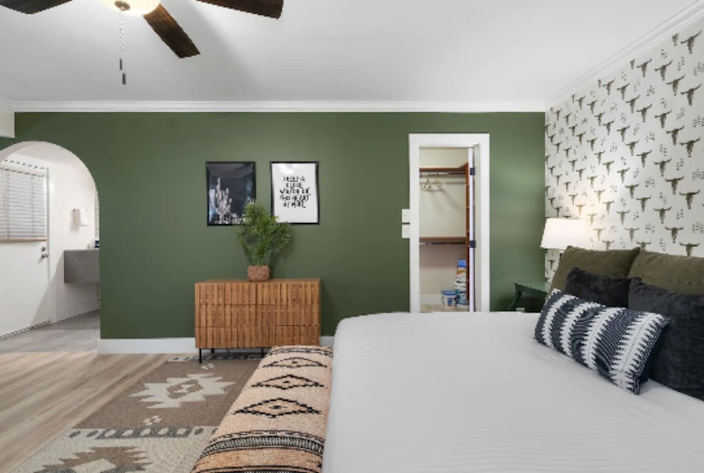 Tucked behind the bed, a walk-in closet and private bath keep this room feeling like its own suite. The olive green wall and framed prints add just enough personality without overwhelming the space.