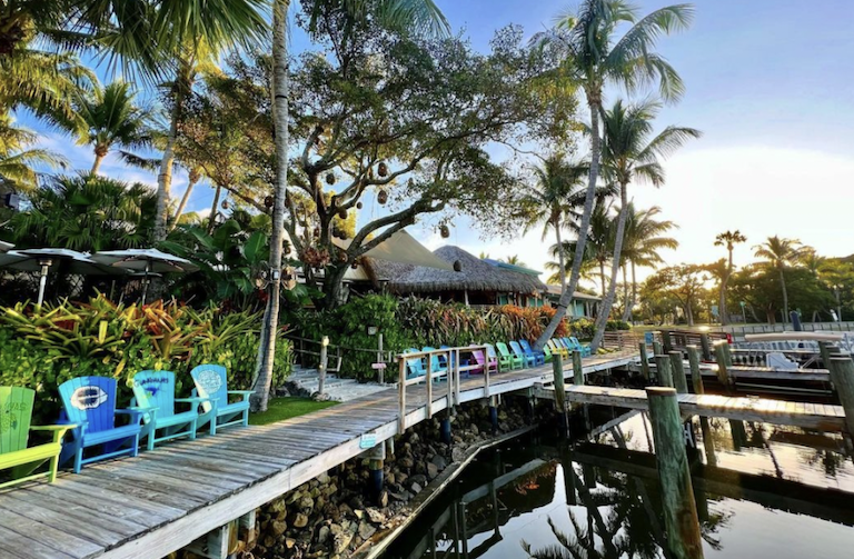 Relax Island-style at Jupiter's iconic waterfront tiki spot, surrounded by lush palms and tropical vibes.  Colorful Adirondack chairs invite you to unwind and soak up the laid-back paradise