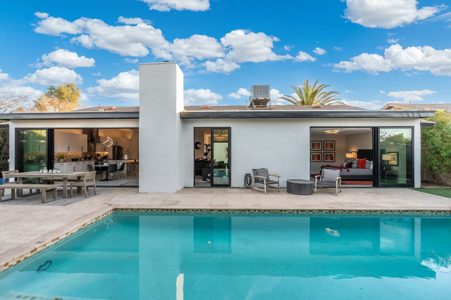 A daytime view of the backyard highlights open-concept living through sliding glass doors and the inviting aqua-blue pool.