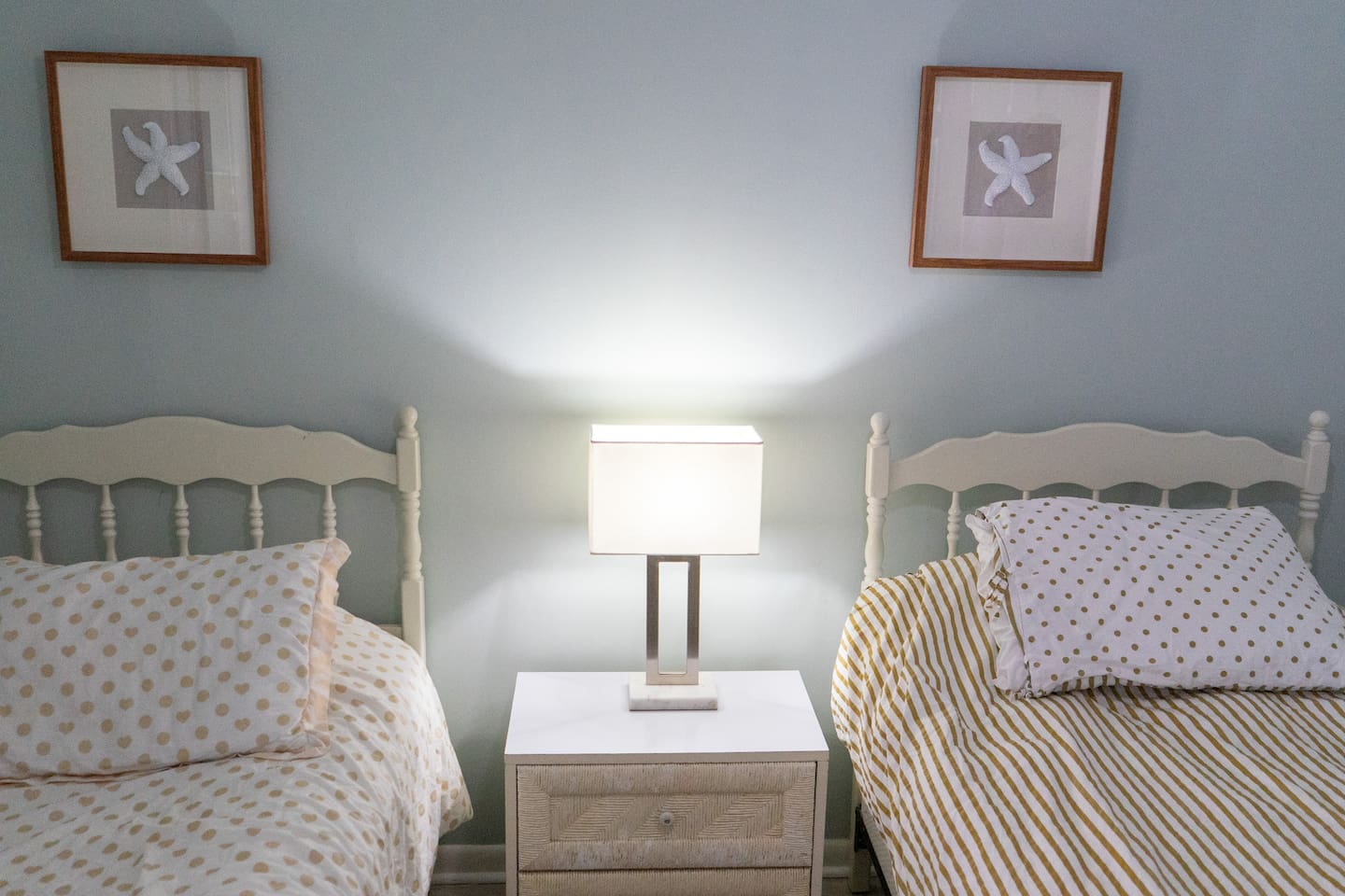 Cozy coastal twin bedroom featuring soft beachy tones, charming starfish artwork, and warm ambient lighting — the perfect retreat after a day in the sand and sun.