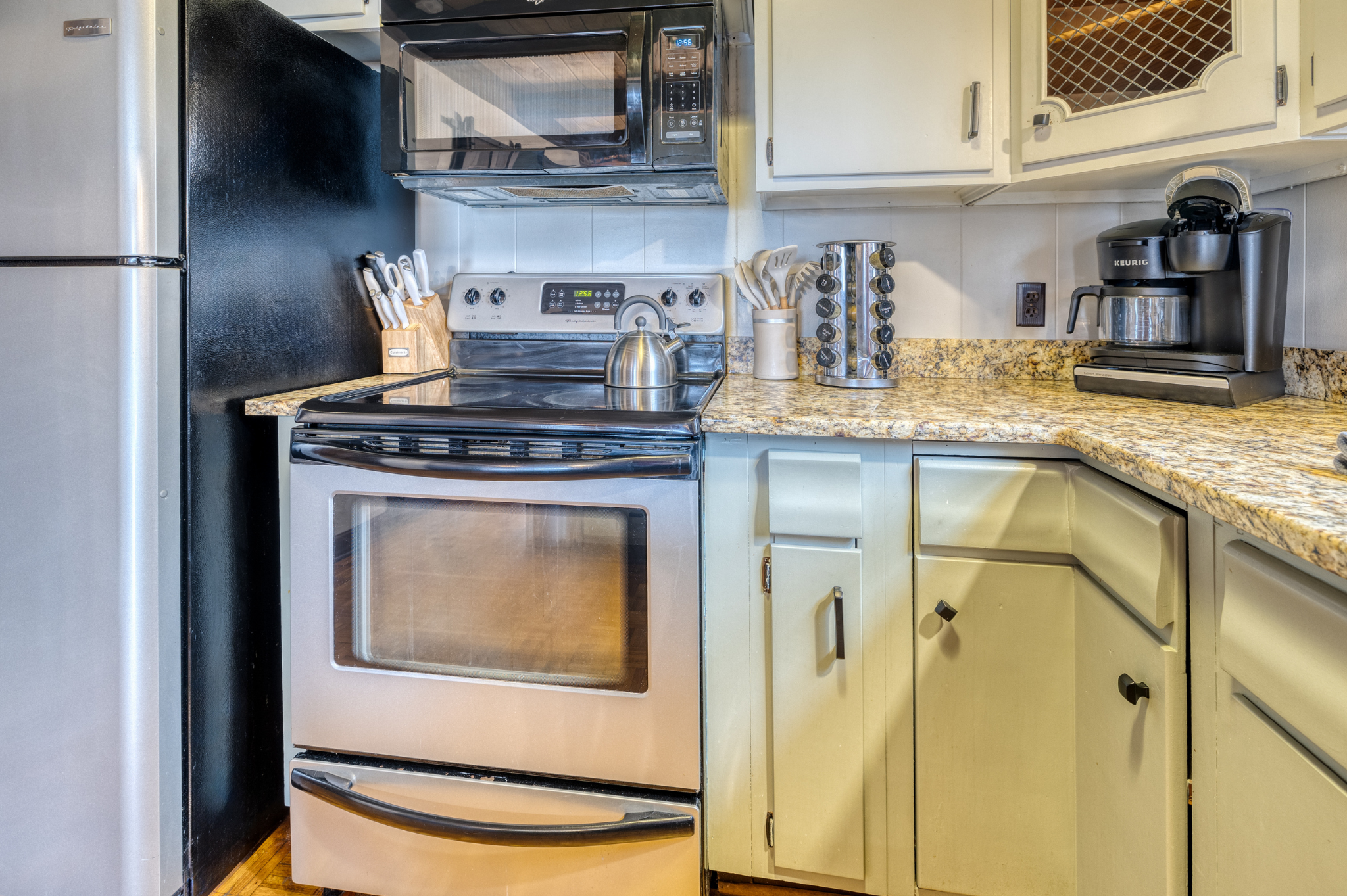 The kitchen features a stainless steel stove, microwave, refrigerator, Keurig coffee maker, and spacious countertop. Bright and inviting with natural light.