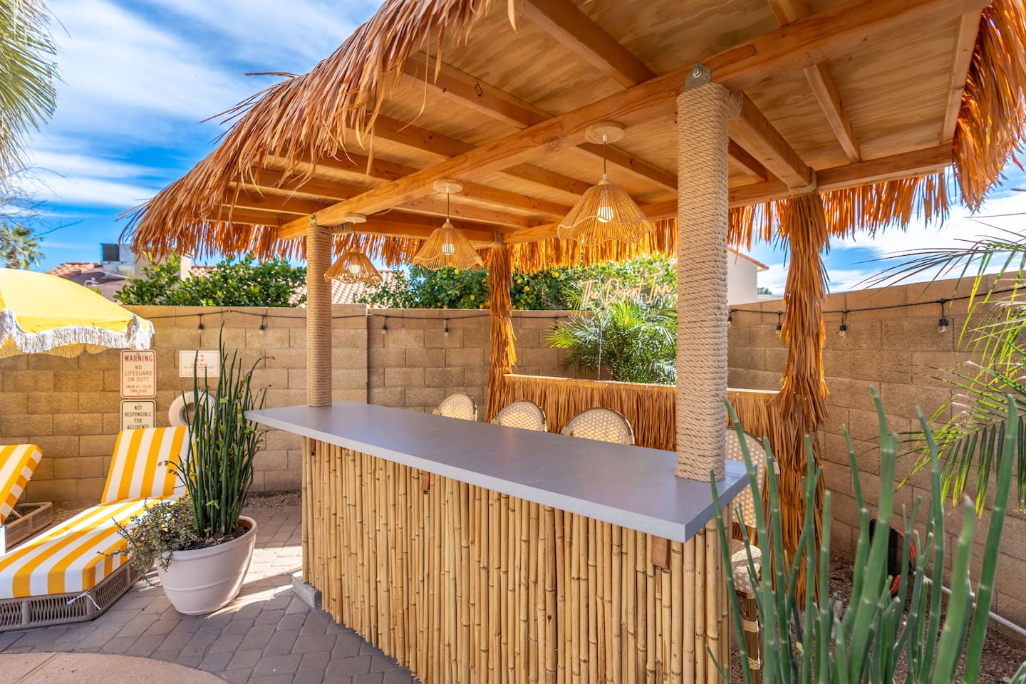 Tropical outdoor bar with thatched roof, pendant lighting, and desert plants—the perfect spot for cocktails and entertaining.