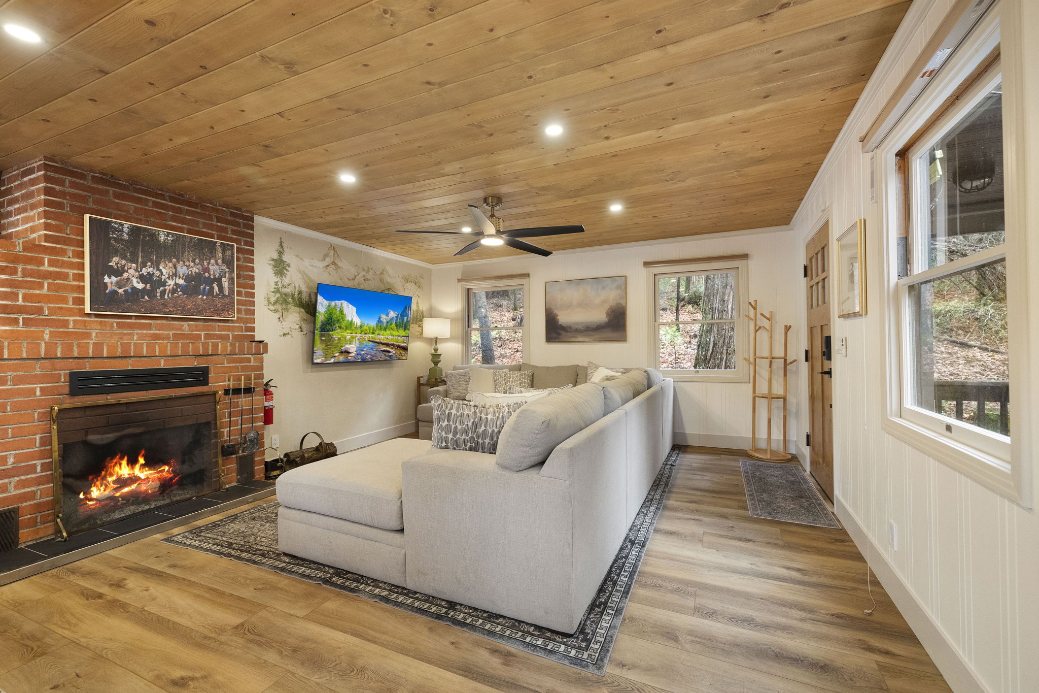 Spacious - yet cozy living room as you walk in. Showcasing a beautiful pine ceiling, lighting options, a large sofa, tv and wood burning fireplace.