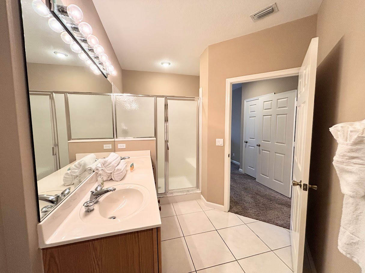 Bright bathroom featuring a large vanity, full mirror, tile flooring, and a walk-in shower with glass doors.