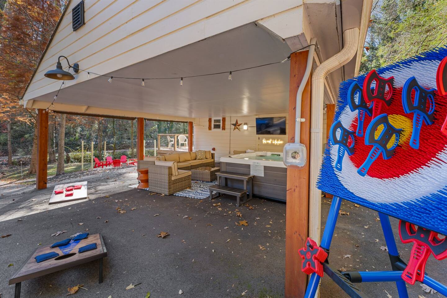 Covered outdoor hangout with hot tub, big-screen TV, lounge seating, and lawn games — perfect for enjoying the fresh air and forest views.