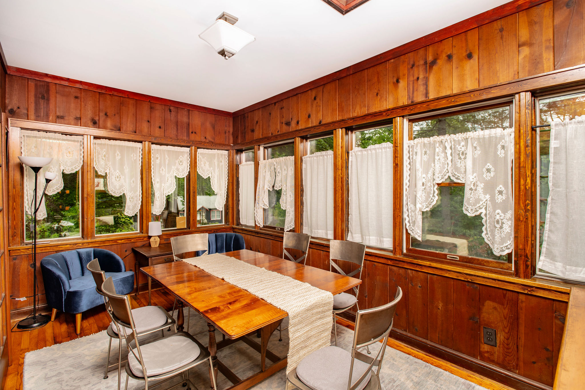 Sunny dining room wrapped in windows, with seating for six and wooded views