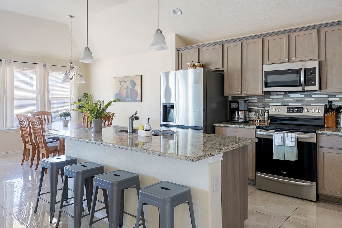 Step into this modern kitchen featuring stainless steel appliances, a sleek granite countertop island with bar stools, and contemporary pendant lighting.