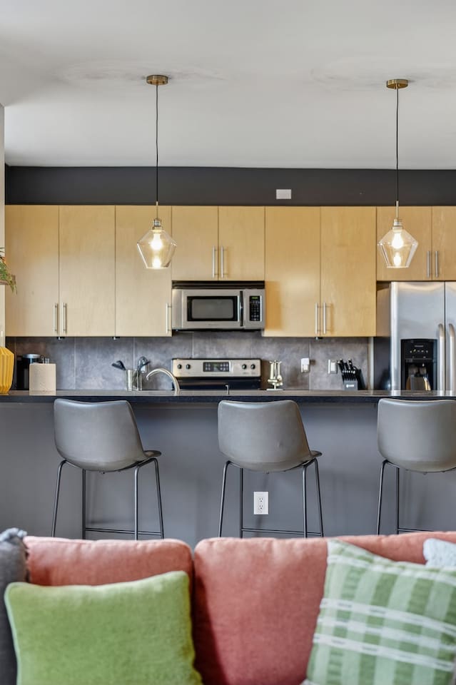 Cook and connect in the open kitchen with stainless steel appliances, sleek bar seating, and designer pendant lighting. Ideal for enjoying coffee, cocktails, or meals together while staying in the heart of downtown Des Moines.