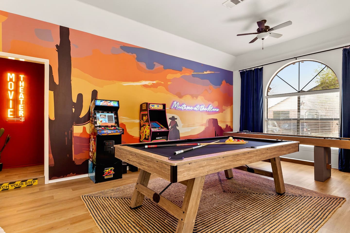 Game room goals—pool table, retro arcade games, mural wall, neon signage, natural light, and movie theater entrance make this a fun-filled retreat for all ages, blending nostalgic charm with modern entertainment in style.
