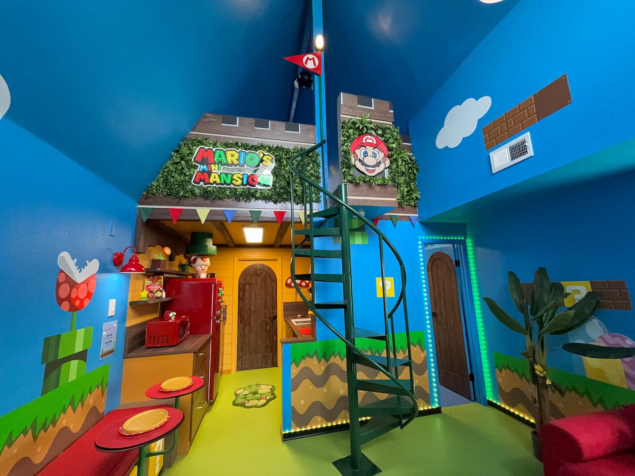Discover the whimsical lower level of Mario's Mini Mansion in Clermont, FL! Green spiral staircase leads to the castle fort with 'Mario's Mini Mansion' sign, red stools, and colorful Super Mario decor throughout. Fun space with kitchenette access.