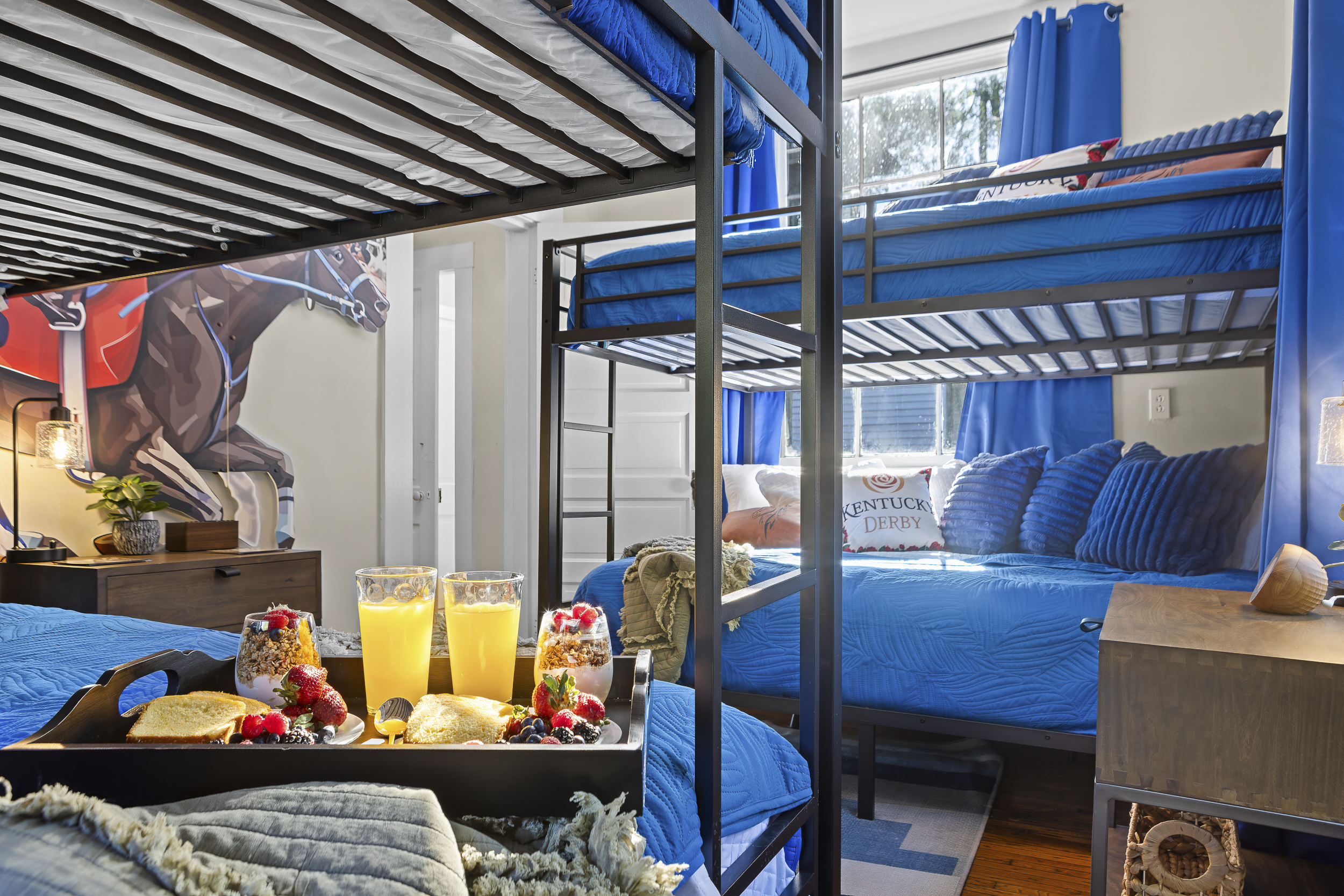 The Kentucky Derby Room from inside. Four bunk spots, blue curtains, and the roar of the crowd on the wall.
