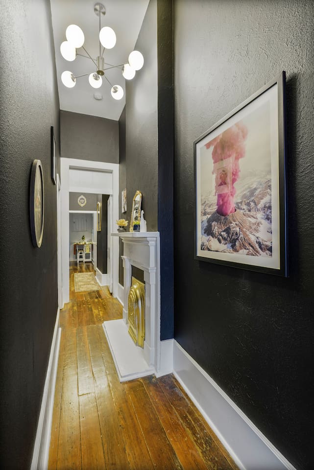 Stroll through this epic hallway with original wood floors, bold art, an exploding pink volcano, and a gold fireplace.