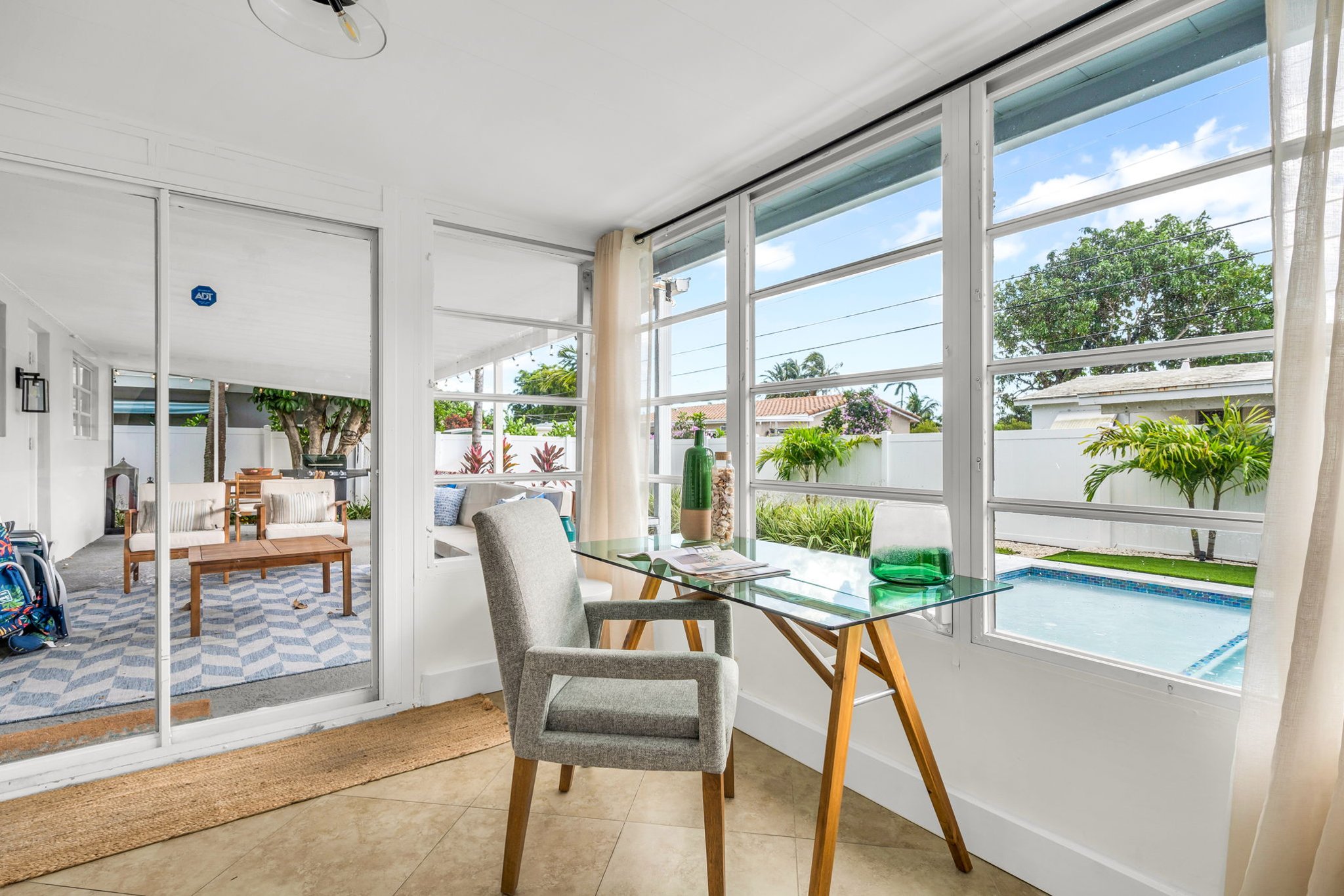 A beautifully designed Florida sunroom with wrap-around windows, modern furnishings, a Smart Fire streaming TV, and tranquil pool views—ideal for lounging, morning coffee, or working in style.