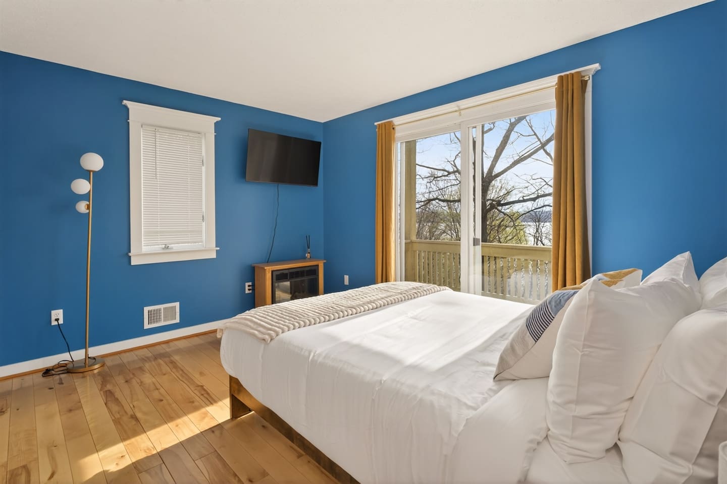 Bright blue master bedroom with stylish artwork, Smart TV, and private balcony access—wake up to peaceful lake views, step outside to sip your morning coffee, and enjoy a calm, relaxing retreat filled with light and comfort